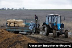 Рабочие едут в кузове трактора с гробами на кладбище в посёлке Старый Крым под Мариуполем, контролируемом Россией. 4 февраля 2023 года