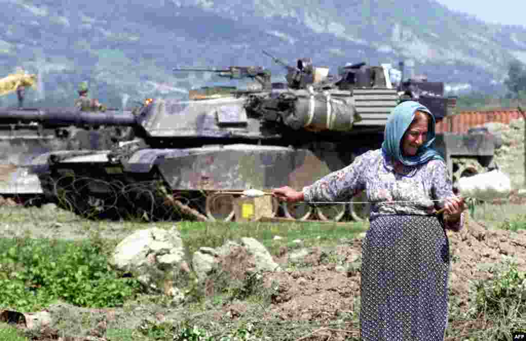 Албанская женщина прядет шерсть перед американским танком M1 Abrams, который участвовал в операции НАТО во время конфликта в Косово, возле авиабазы Ринас, 12 мая 1999 года. С экипажем из четырех человек (командир, наводчик, заряжающий и механик-водитель) «Абрамс» является одним из самых тяжелых танков, находящихся на вооружении, его масса составляет почти 62 тонны.